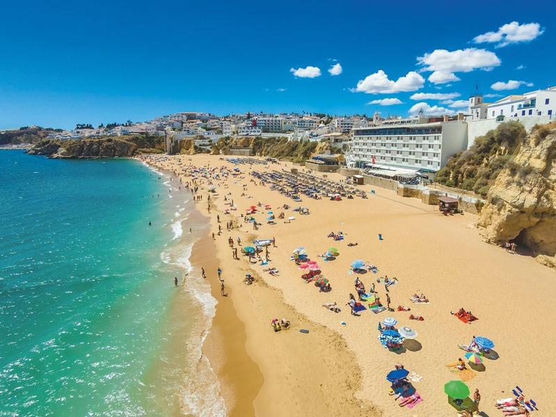 Plaża z złotym piaskiem, kolorowymi parasolami i hotelami na klifach pod czystym niebem