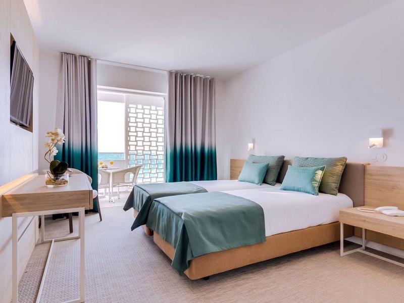 Nowoczesny pokój hotelowy z dużym łóżkiem, drewnianymi meblami i balkonem z widokiem na miasto.