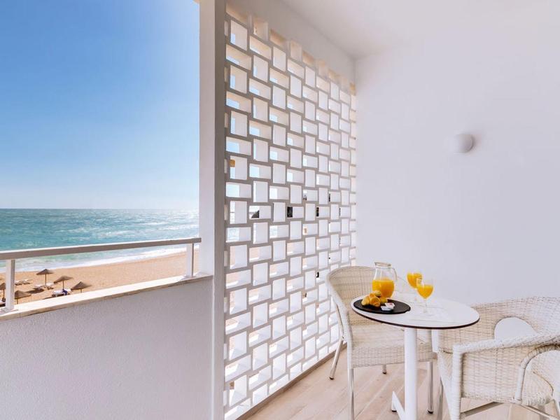 Balkon z małym okrągłym stołem, dwoma krzesłami, napojami i widokiem na morze.