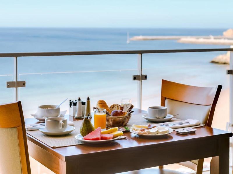 Przytulny stół na śniadanie na balkonie z widokiem na morze i przeszkloną balustradą.