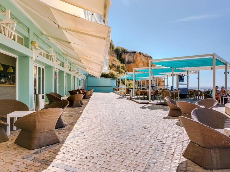 Kawiarnia na świeżym powietrzu przy wybrzeżu z wiklinowymi krzesłami i markizami pod czystym niebem.