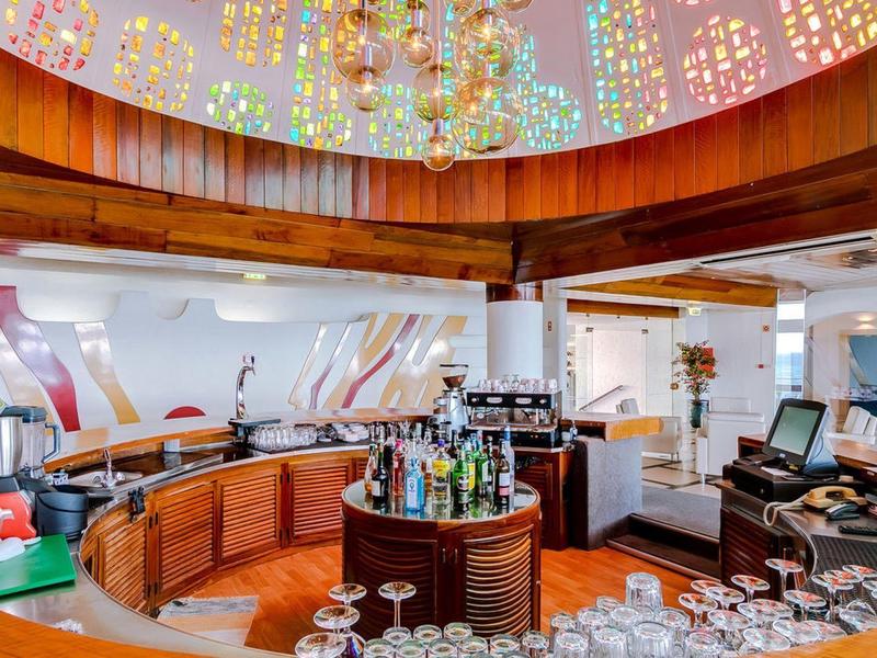 Nowoczesny bar hotelowy z kolorowymi żyrandolami, drewnianym barem i miejscami do siedzenia w jasnym pomieszczeniu.