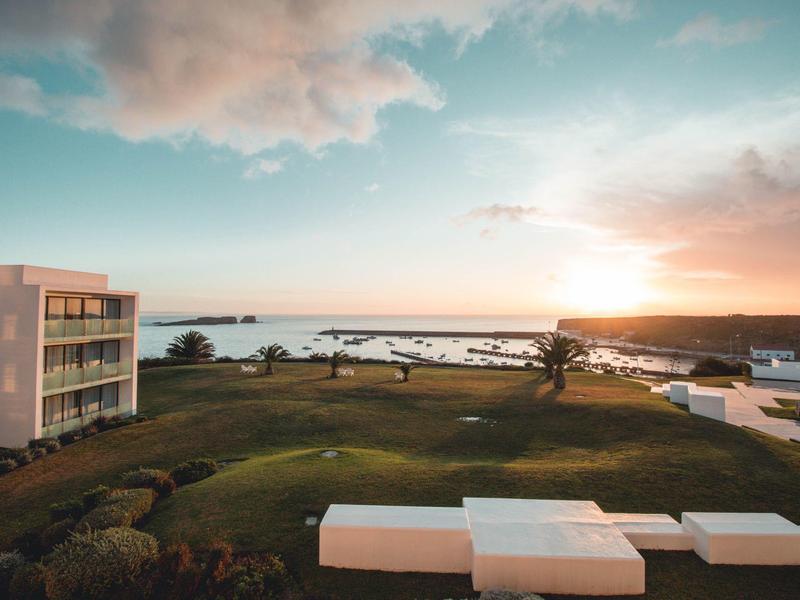 Pohled na hotel u vody s trávníkem a loděmi při západu slunce.