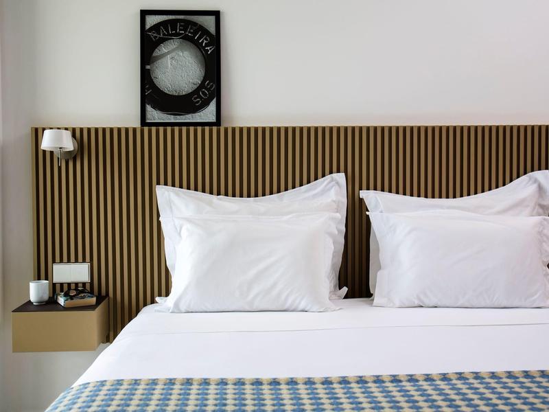 Moderní hotelový pokoj se dvěma bílými polštáři a dřevěným čelem postele.