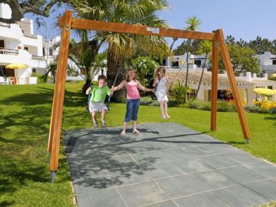 Drei Kinder schaukeln auf einem Holzgarten-Schaukelgerüst bei sonnigem Wetter.