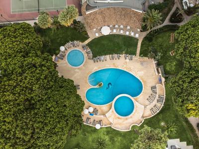 Außenpool in organischer Form mit Liegestühlen und viel Grün rundherum.