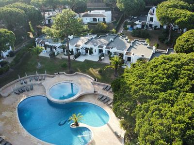 Luftaufnahme eines Hotelpools umgeben von Bäumen und weißen Gebäuden in einer grünen Anlage.