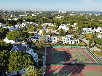 Luftaufnahme einer Hotelanlage mit weißen Gebäuden, Tennisplätzen und grüner Umgebung.