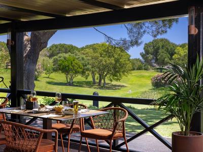 Gemütlicher Essbereich im Freien mit Blick auf grünen Golfplatz und Bäume