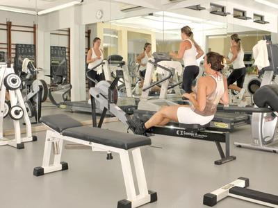 Innenansicht eines voll ausgestatteten Fitnessstudios mit mehreren Personen beim Training.