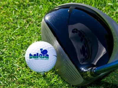 Golfball mit Hotel-Logo auf grünem Gras neben einem schwarzen Golfschläger