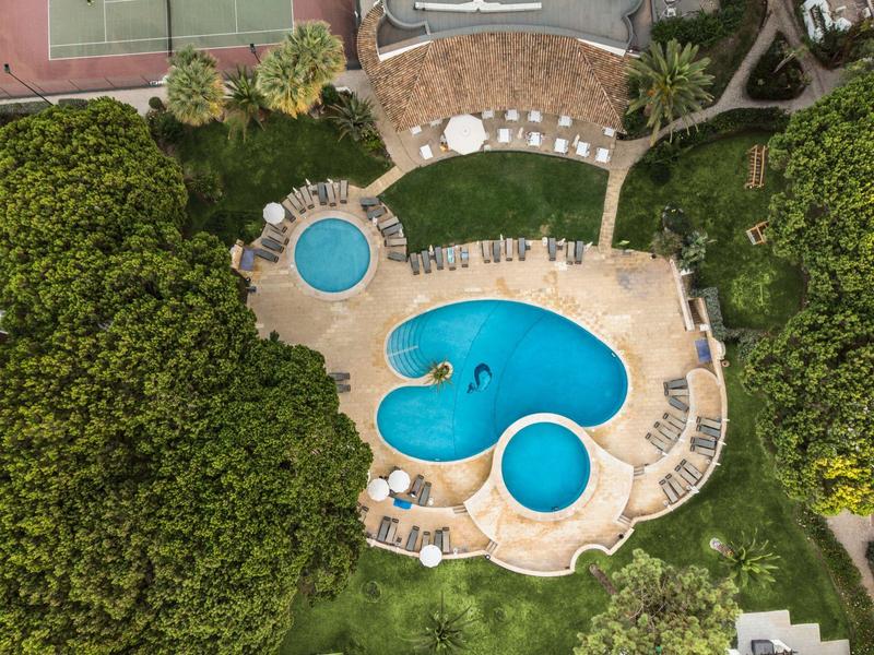 Außenpool in organischer Form mit Liegestühlen und viel Grün rundherum.