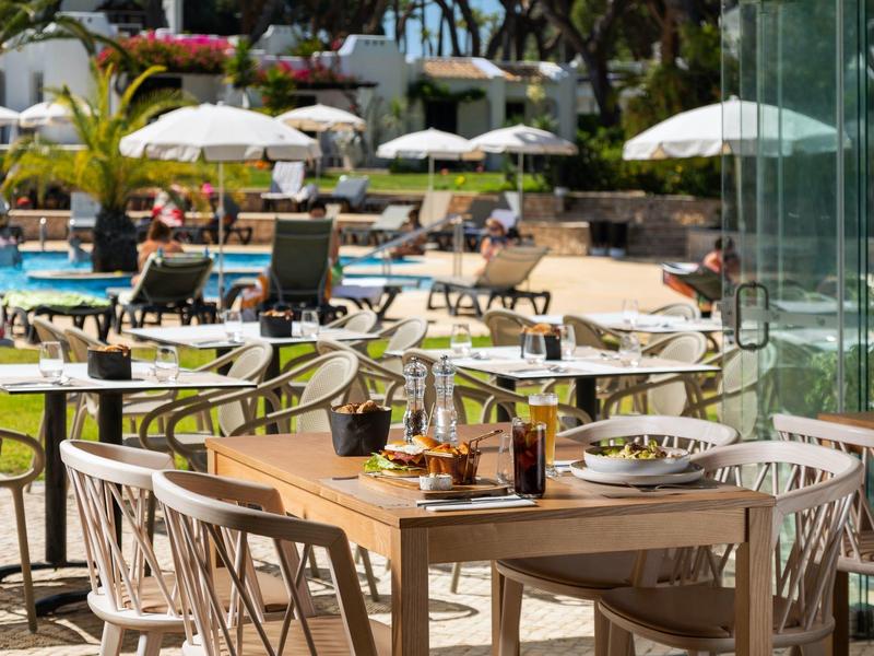 Hotelterrasse mit gedeckten Tischen und Liegestühlen am sonnigen Poolbereich