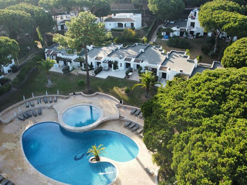 Luftaufnahme eines Hotelpools umgeben von Bäumen und weißen Gebäuden in einer grünen Anlage.