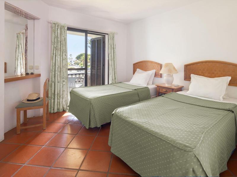 Hell eingerichtetes Hotelzimmer mit zwei Einzelbetten und bodentiefem Fenster mit Balkon