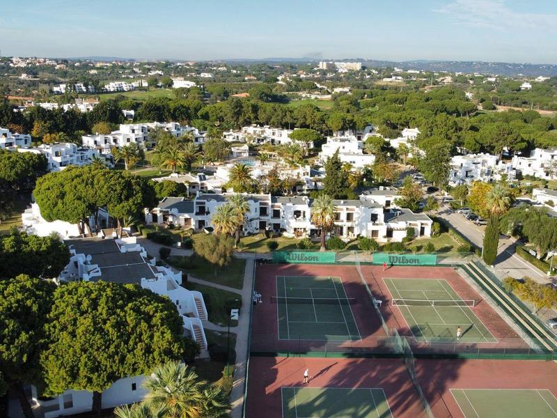 Luftaufnahme einer Hotelanlage mit weißen Gebäuden, Tennisplätzen und grüner Umgebung.