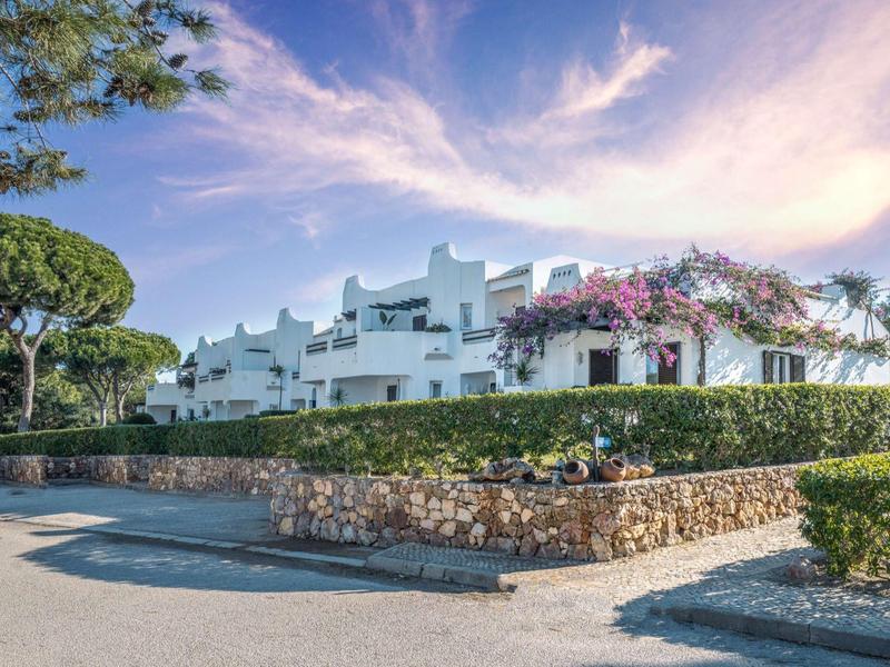 Weißes Hotelgebäude mit blühenden Pflanzen und umgeben von Grün unter blauem Himmel.