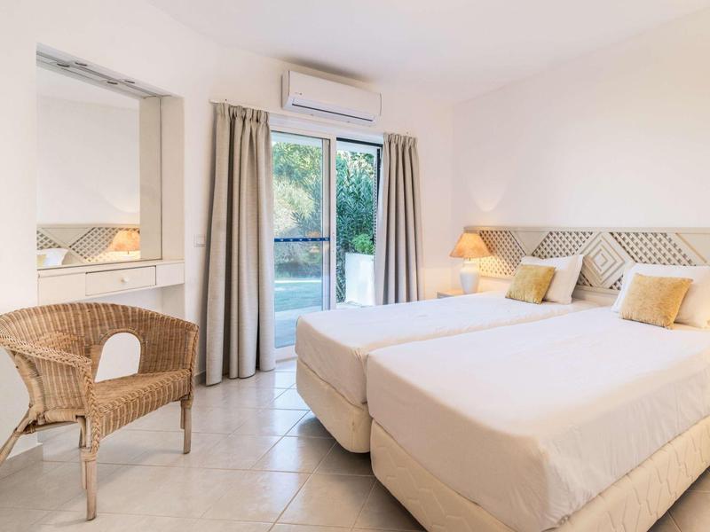 Helles Hotelzimmer mit zwei Einzelbetten, Terrasse und Rattanstuhl.