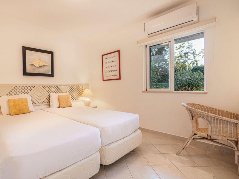 Hell eingerichtetes Hotelzimmer mit zwei Einzelbetten, einem Fenster und einfachem Mobiliar.