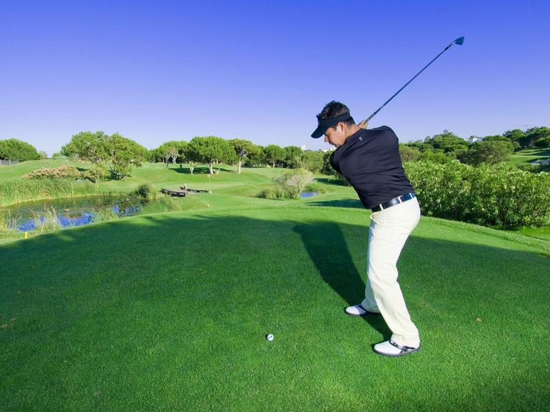 Mann im Sportoutfit bereitet sich auf den Golfschwung vor auf grünem Golfplatz bei klarem Himmel.