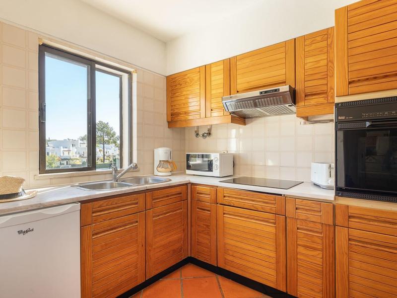 Moderne Küche mit Holzmöbeln, weißem Geschirrspüler, Mikrowelle und Fenster mit Außenblick.