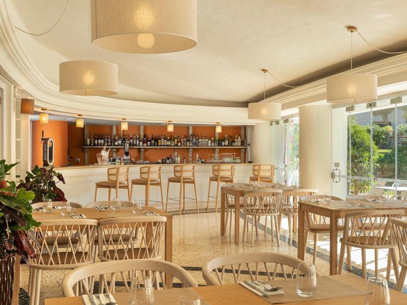 Helles Restaurant mit Holzmöbeln, Theke und großen Fenstern mit Blick ins Grüne.