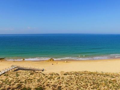 Breiter Sandstrand mit klarem blauem Himmel und türkisfarbenem Meer, Dünen im Vordergrund.