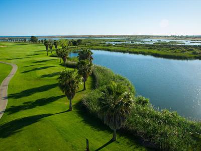 Zelené golfové hřiště vedle klidného jezera pod jasnou modrou oblohou.