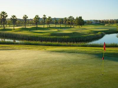 Golfové hřiště se zeleným fairwayem, vodní překážkou a červenou vlajkou za západu slunce.