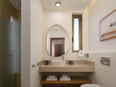 Helles Badezimmer mit ovalem Spiegel, Waschbecken, Fön und zwei Handtüchern unter der Ablage.