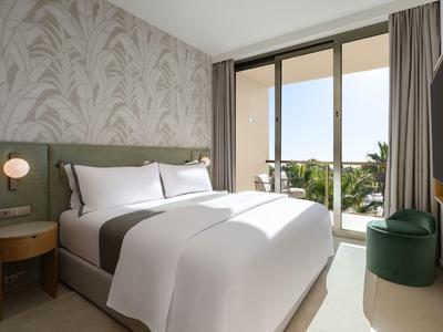 Helles, modernes Schlafzimmer mit Doppelbett, Tapetenmuster, Balkon und Blick auf Palmen.