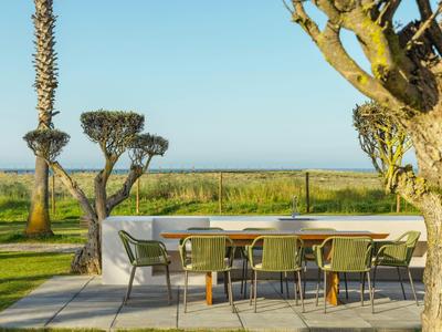 Moderner Gartentisch mit Stühlen auf Terrasse, umgeben von Bäumen, Wiese und blauem Himmel.