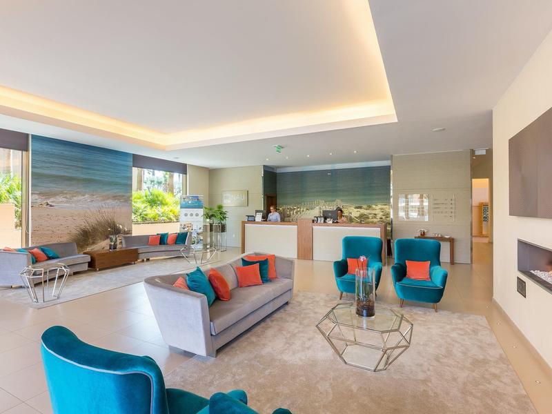 Helles Wohnzimmer mit moderner Einrichtung, blauen Sesseln, grauem Sofa und großem Fenster.