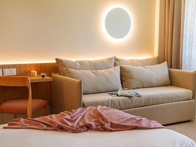 Modern eingerichtetes Hotelzimmer mit Sofa, Bett und rundem Wandlicht.