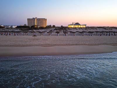 Strand mit ruhigem Meer, mehreren Regenschirmen und zwei Hotels im Sonnenuntergang.