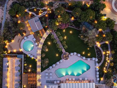 Nächtliche Ansicht eines beleuchteten Hotelpools mit umgebenden Liegestühlen und Grünflächen.