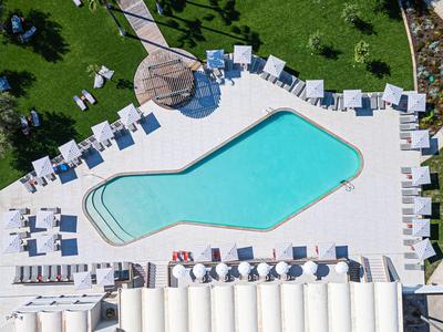 Ein Swimmingpool in ungewöhnlicher Form umgeben von Liegestühlen und grüner Rasenfläche.
