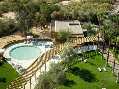 Hotelanlage mit rundem Pool, Liegestühlen, grünen Rasenflächen und Palmen.