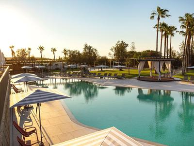 Ein großer Pool mit Liegestühlen und Palmen in einer Hotelanlage bei Sonnenuntergang.