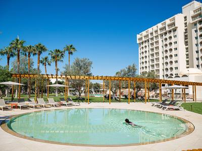 Runder Pool im Hotelgarten mit Liegestühlen und Palmen unter blauem Himmel.