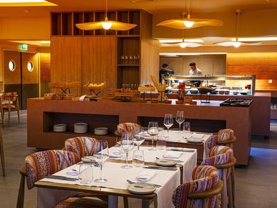 Modernes Restaurant mit gedeckten Tischen und offener Küche in warmen Holztönen.