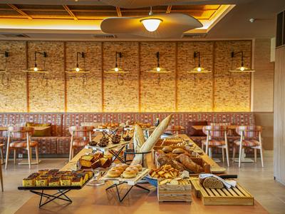 Hell eingerichtetes Café mit Backwarenbuffet und Sitzbereich vor einer Backsteinwand.