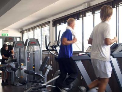 Drei Personen trainieren auf Laufbändern in einem modernen Fitnessraum mit großen Fenstern.