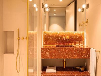 Moderne Hoteldusche mit goldener Armatur und eleganter rotbrauner Marmorwaschbeckenplatte.