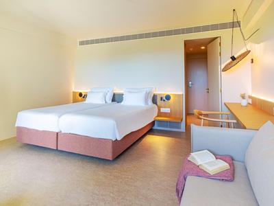Modern eingerichtetes Hotelzimmer mit Doppelbett, Sofa und hellen Wänden.
