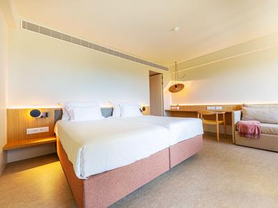 Helles Hotelzimmer mit Doppelbett, Couch, Schreibtisch und warmen Holzdetails.