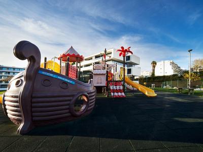 Moderní dětské hřiště s pirátskou lodí a skluzavkami v hotelové zahradě.