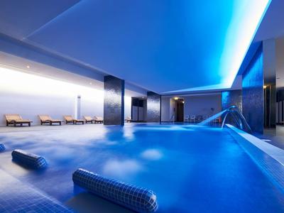 Moderní vnitřní bazén s modrým osvětlením a odpočinkovými zónami v hotelu.