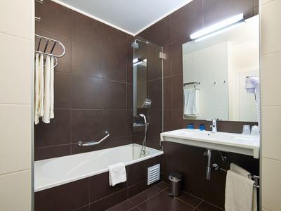 Moderní koupelna s hnědými dlaždicemi, vanou, zrcadlem a umyvadlem.