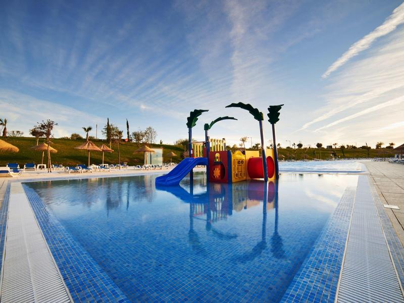 Barevné vodní hřiště v bazénu u letoviska pod jasnou oblohou.